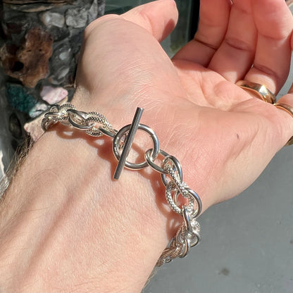 A silver toggle clasp link bracelet.  Some of the links are textured, and others are polished.  The toggle ring is stamped "India."