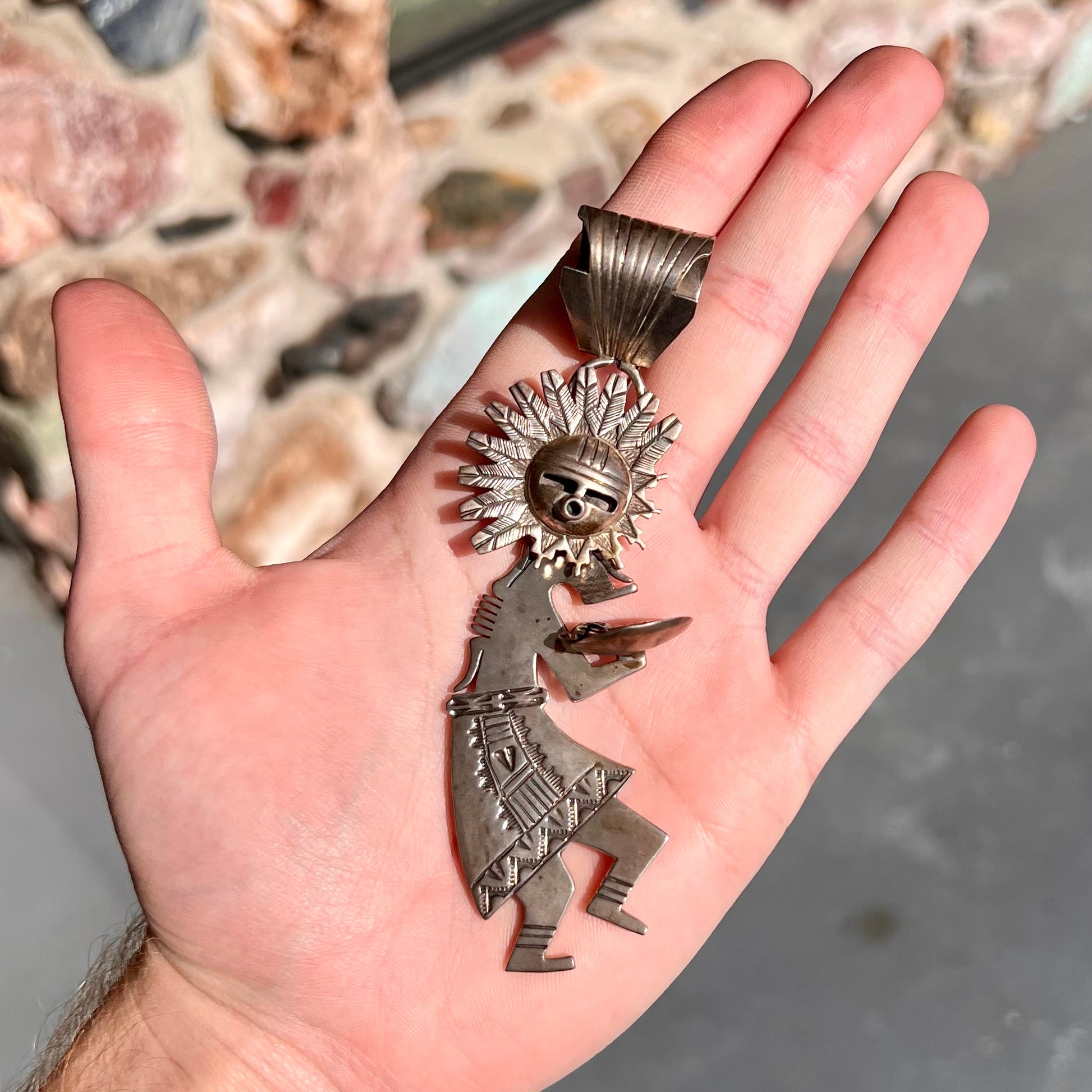 A "Navajo Sunface" kachina doll pendant made from sterling silver by artist Bennie Ration.  The piece measures four and a half inches long.