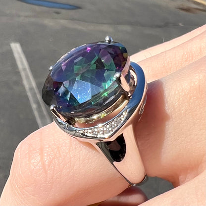 A large, round cut pink and green mystic topaz set in a sterling silver ring with white topaz accent stones.