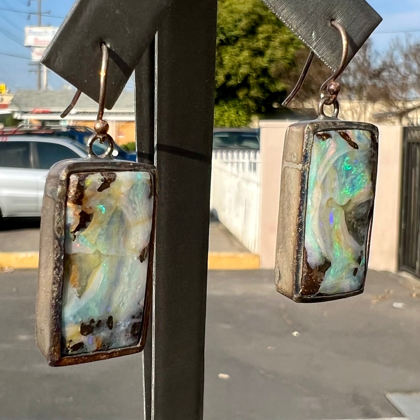 A pair of handmade sterling silver boulder opal earrings.  The earrings dangle from French wire hooks.