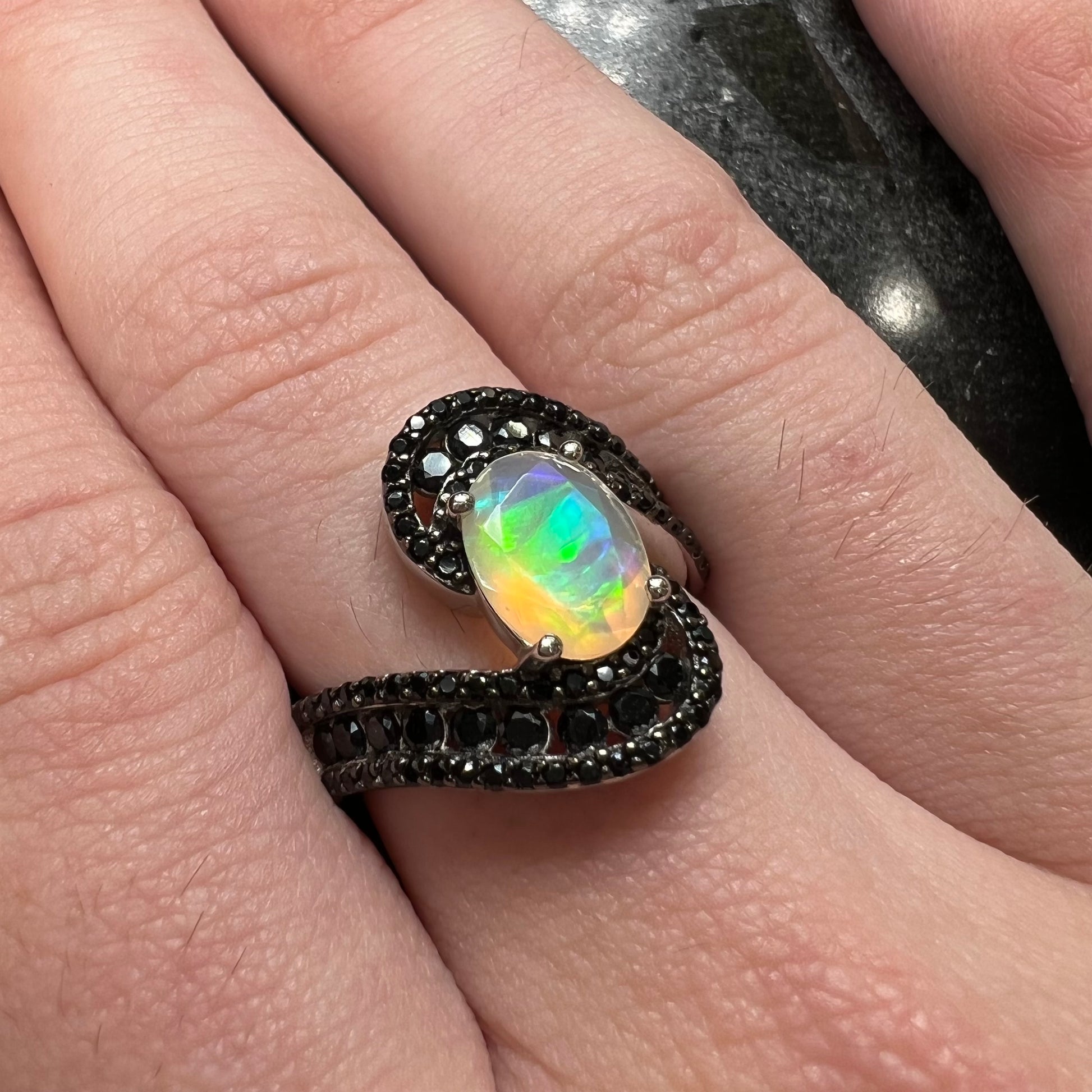 A sterling silver ring set with round black spinel stones and an oval cut, faceted Ethiopian opal.
