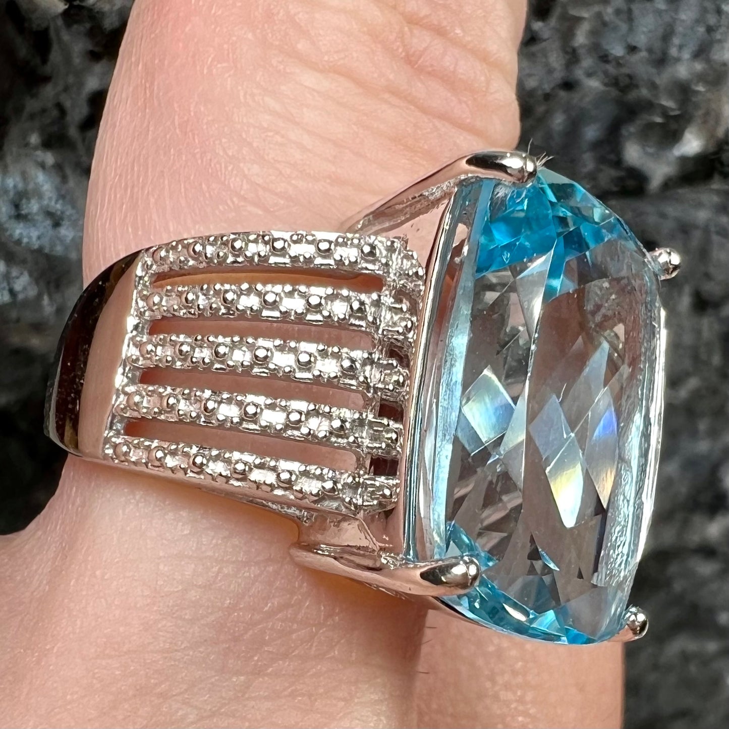 A sterling silver ring prong set with a large, cushion cut sky blue topaz stone.  The shank has been textured to mimic accent stones.