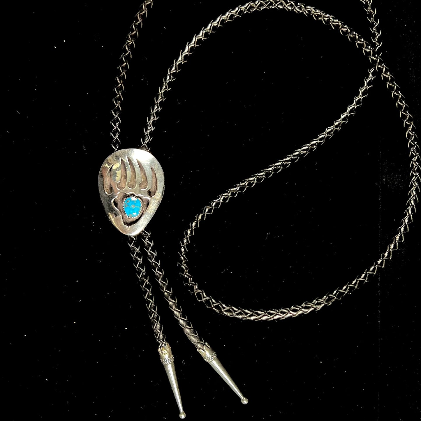 A sterling silver bolo tie in the shape of a bear's paw set with a Morenci turquoise stone.