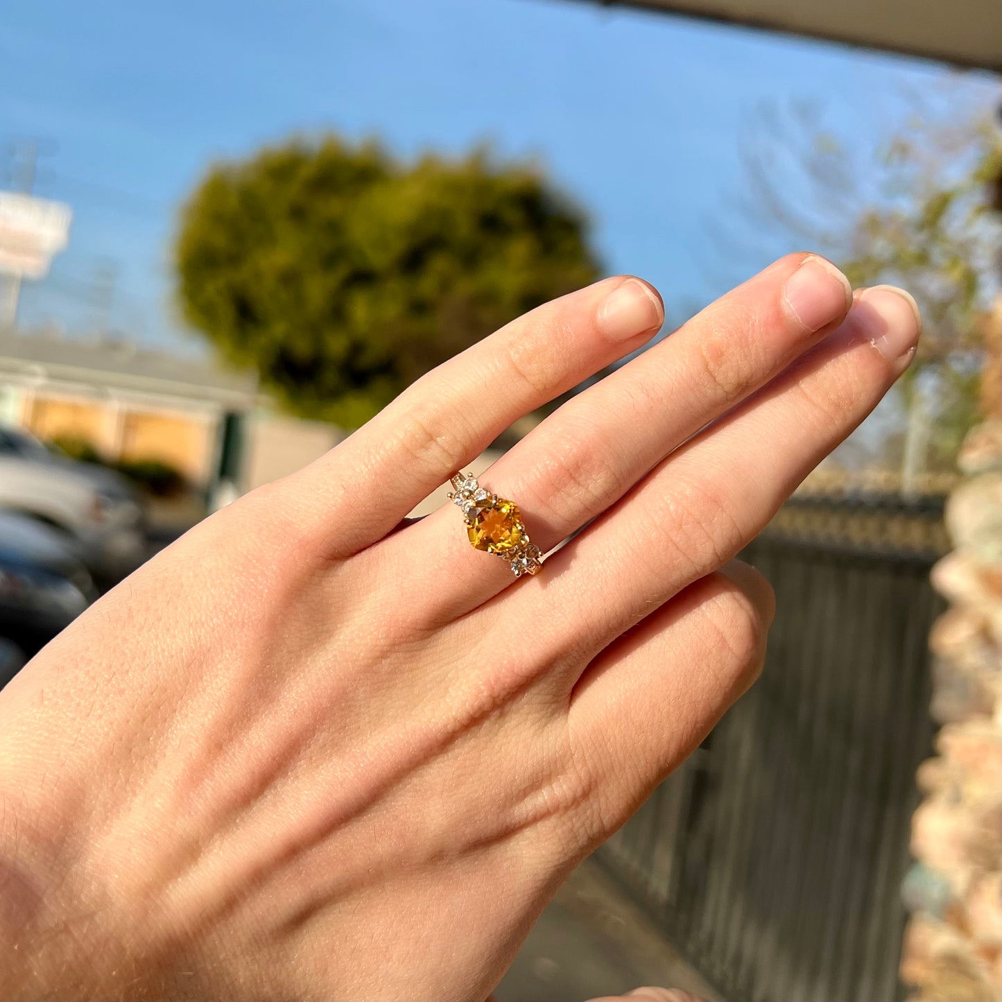 A cushion cut citrine set in a yellow gold ring with four round white sapphires and two diamonds on each side.