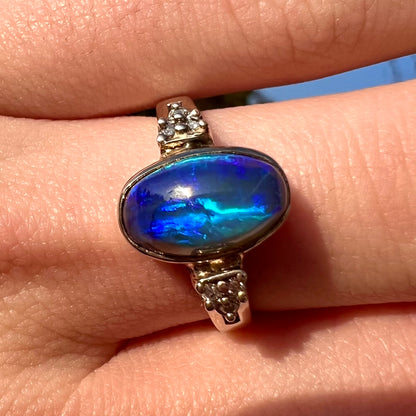 A white gold ring set with a Lightning Ridge black opal and diamond accents.  The opal displays a cat's eye pattern.  Mary Eunice style shank