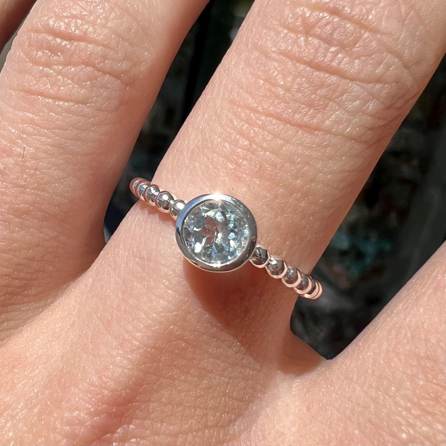 A silver, bezel set, round cut sky blue topaz solitaire ring.  The band is made of connected silver balls.