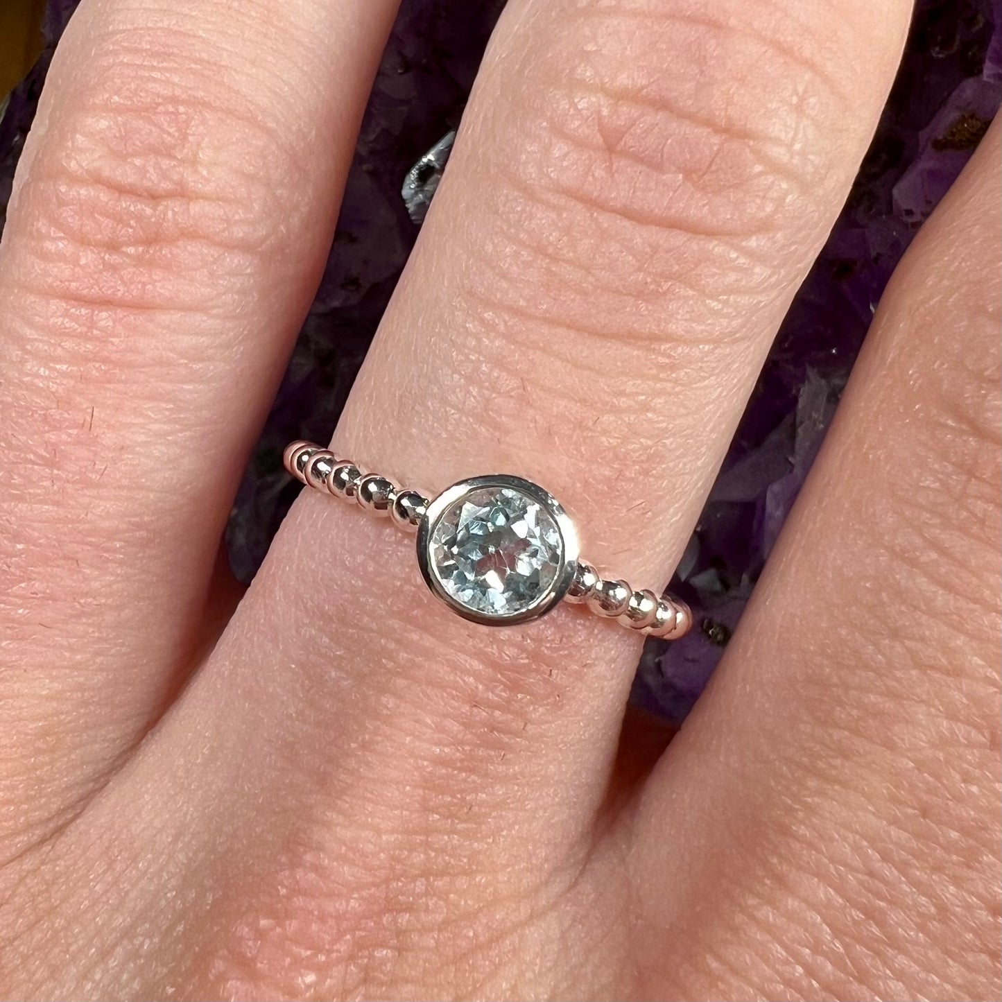 A silver, bezel set, round cut sky blue topaz solitaire ring.  The band is made of connected silver balls.