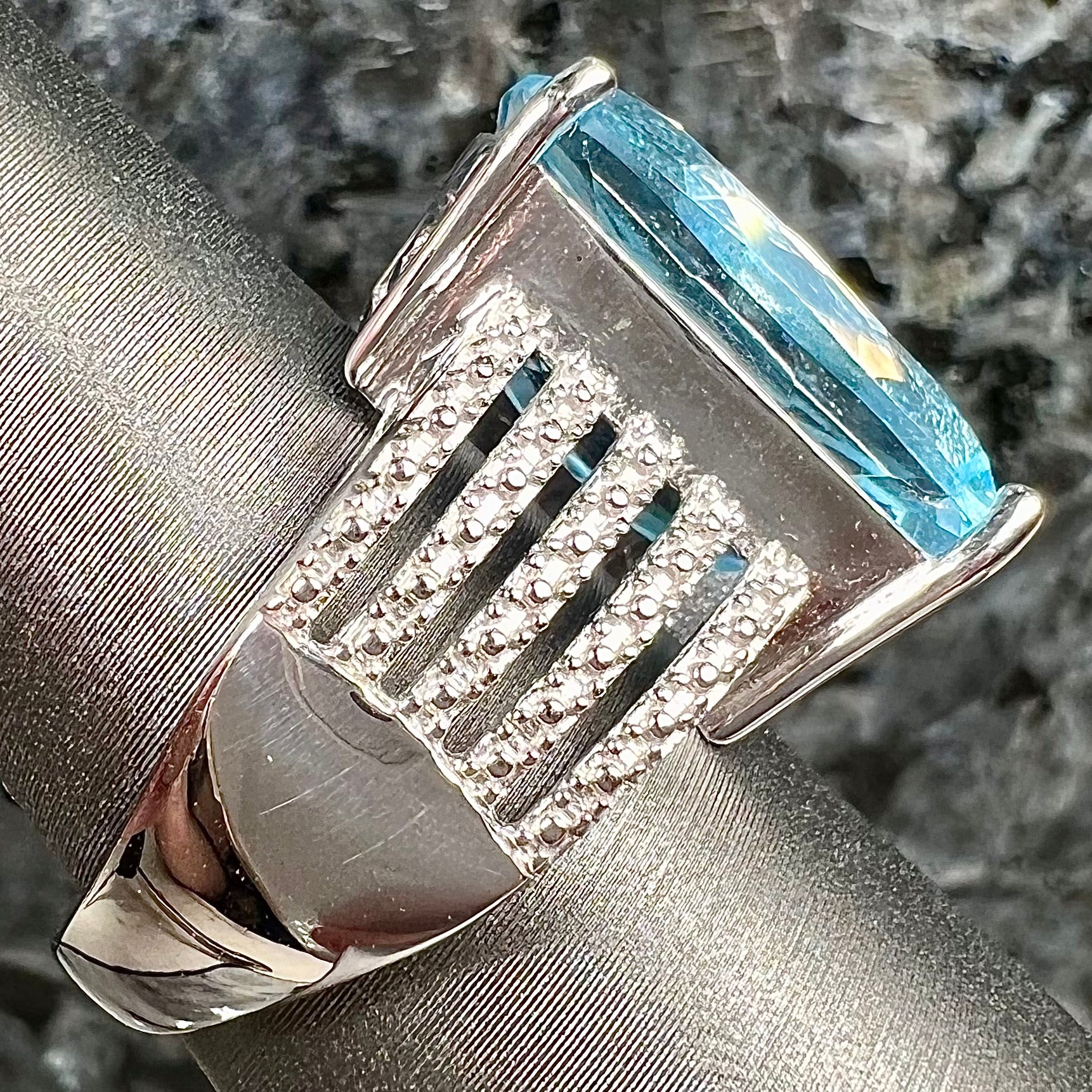 A sterling silver ring prong set with a large, cushion cut sky blue topaz stone.  The shank has been textured to mimic accent stones.