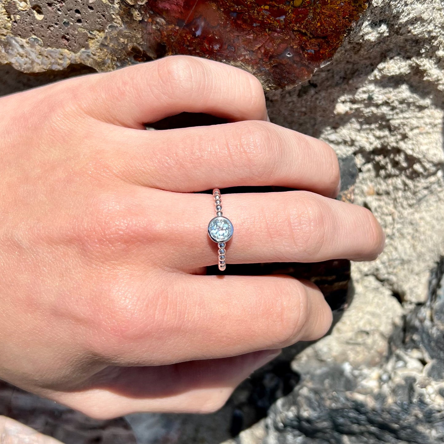 A silver, bezel set, round cut sky blue topaz solitaire ring.  The band is made of connected silver balls.