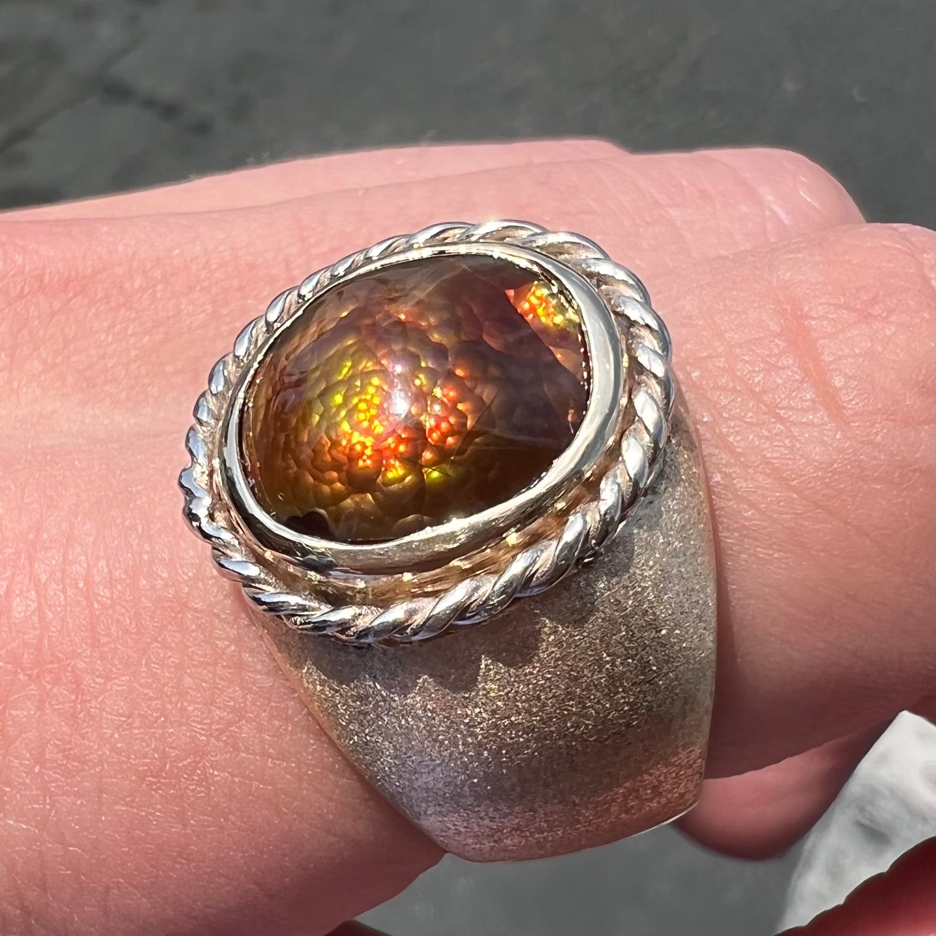 A men's matte finish textured gold fire agate ring.  There is a gold rope bezel around the oval cabochon cut stone.