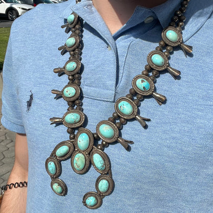 A silver Navajo style unisex squash blossom necklace set with oval cut Sleeping Beauty turquoise stones.