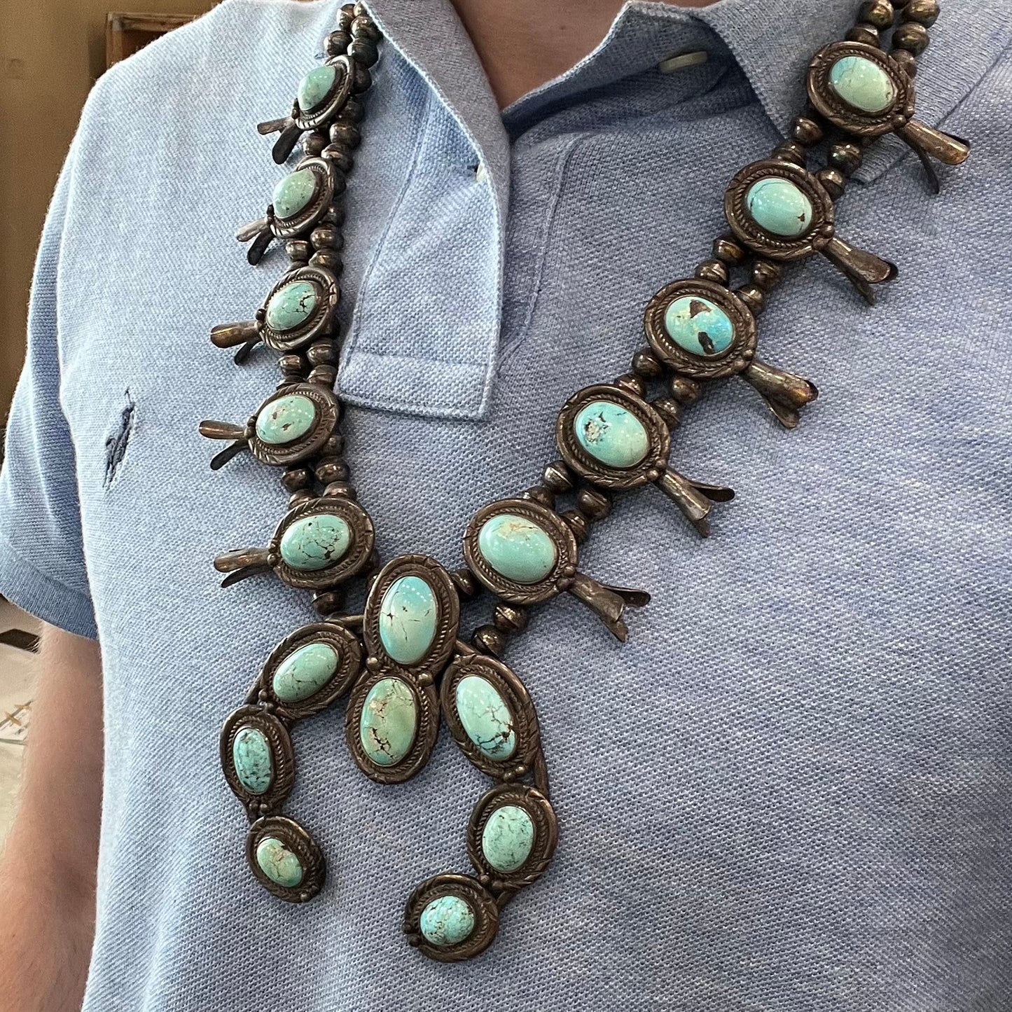 A silver Navajo style unisex squash blossom necklace set with oval cut Sleeping Beauty turquoise stones.