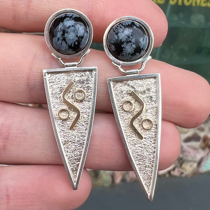 A pair of two-tone silver and gold snowflake obsidian earrings handmade by Zuni artist, Myron Panteah.