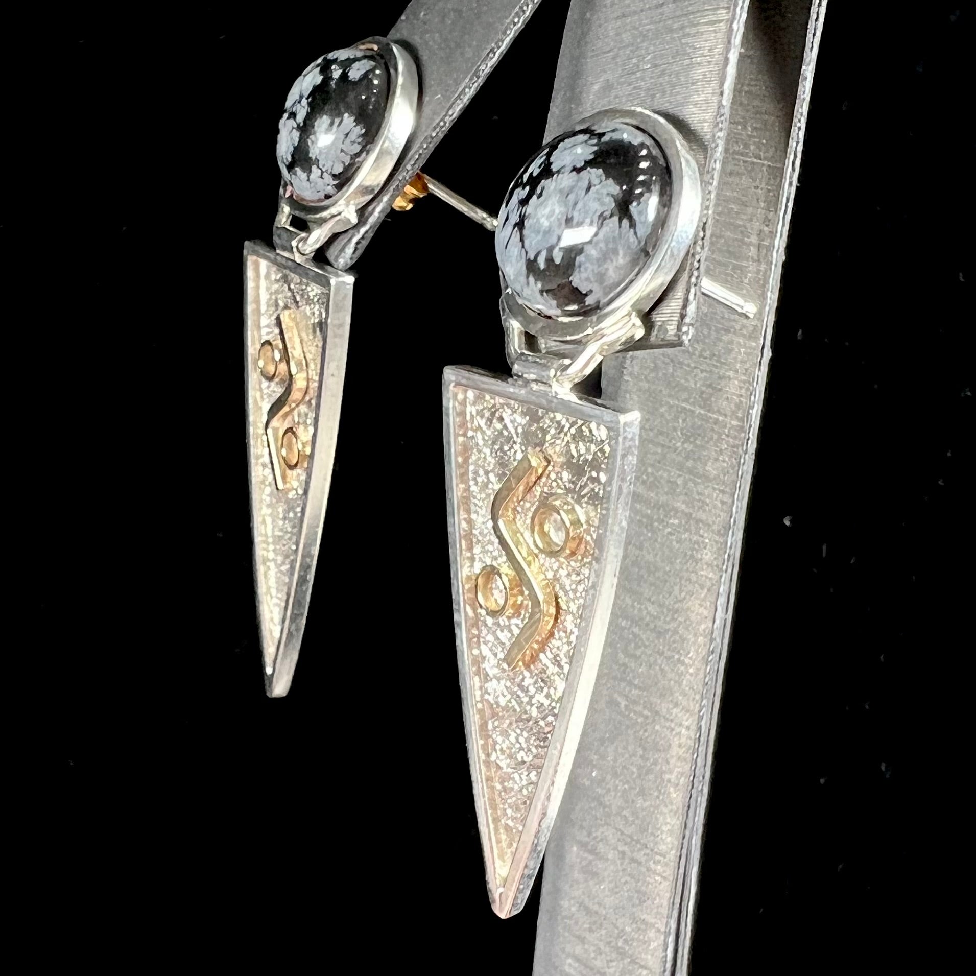 A pair of two-tone silver and gold snowflake obsidian earrings handmade by Zuni artist, Myron Panteah.