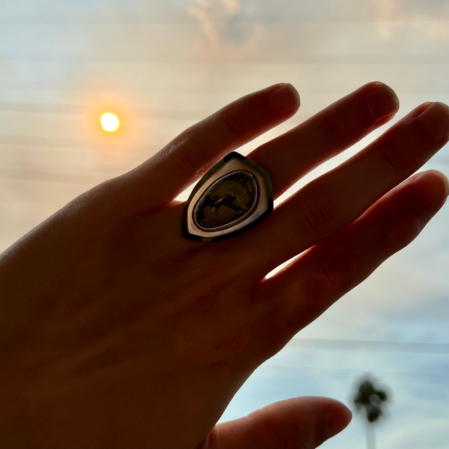 A hand wearing a gaspeite ring covering smoke blocked sun in Southern California.