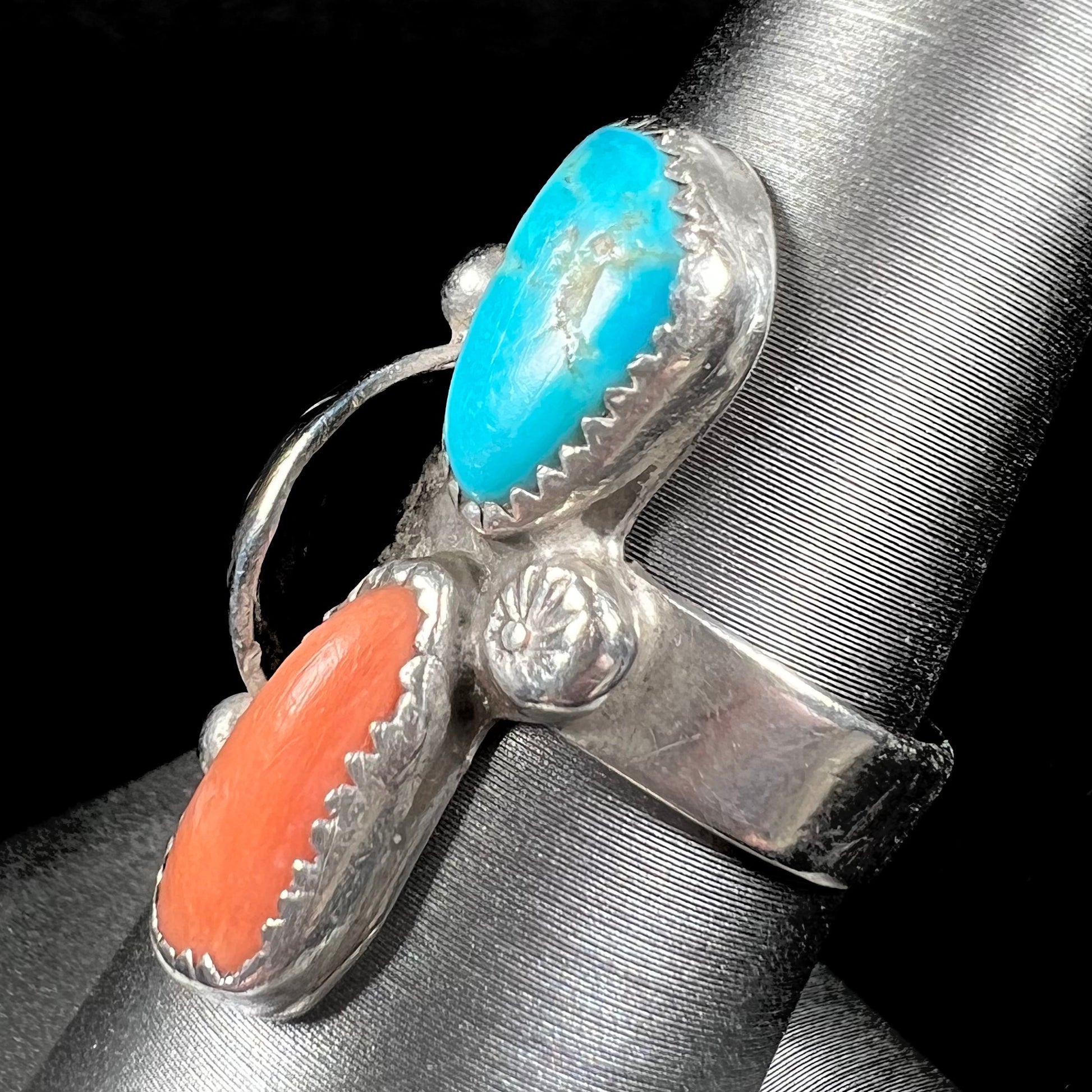 A Navajo silver ring set with turquoise and coral stones.  The ring has a feather decoration.
