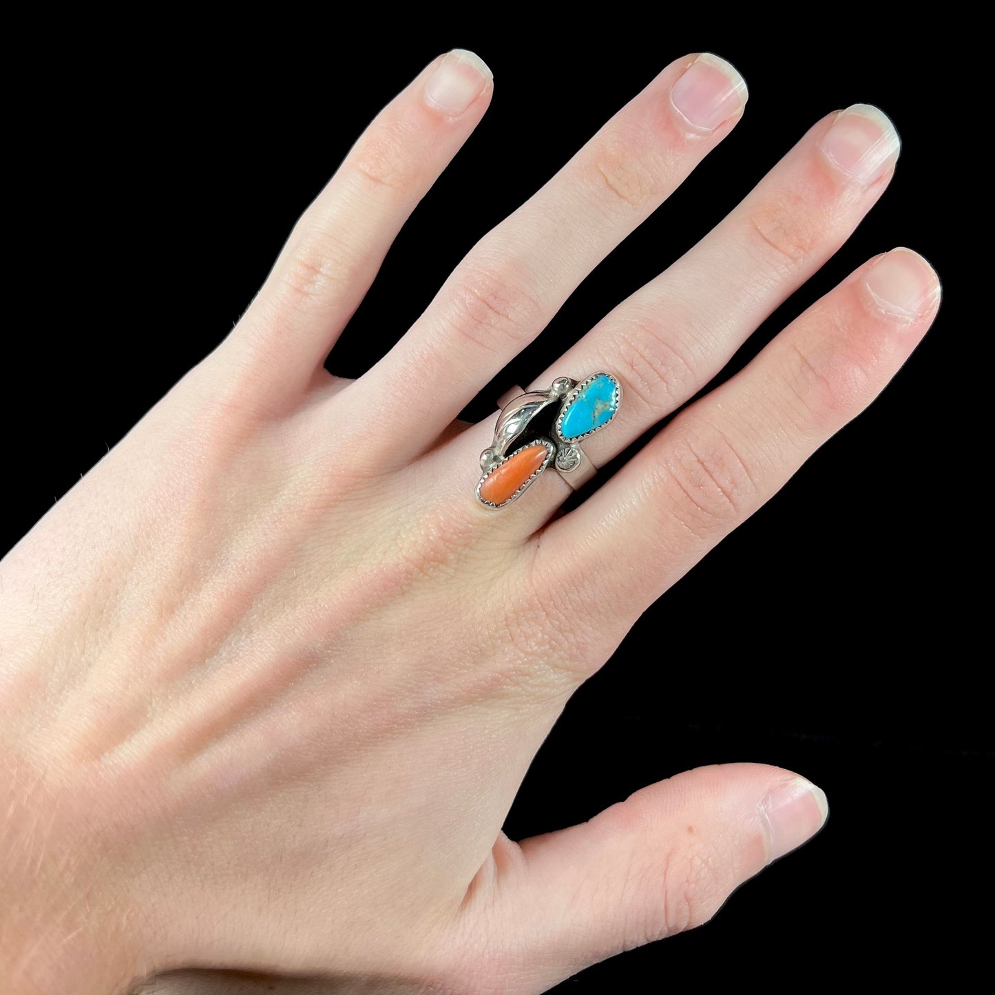 A Navajo silver ring set with turquoise and coral stones.  The ring has a feather decoration.