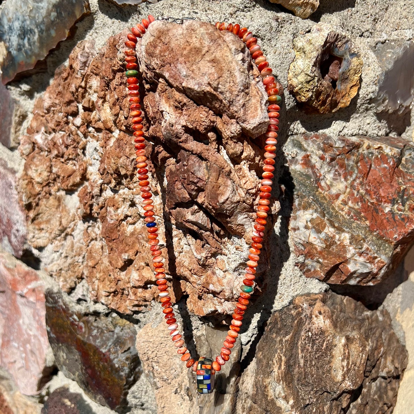 A handmade seashell pendant inlaid with spiny oyster, mother of pearl, and lapis lazuli on a spiny oyster bead necklace by Charlene Reano.