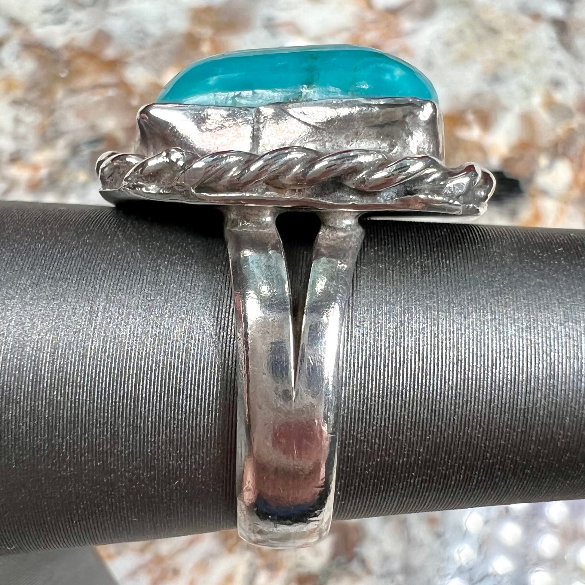 A sterling silver turquoise split shank ring.  There is a handmade silver rope around the turquoise.