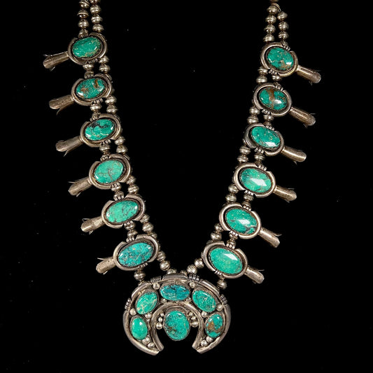 A silver Kingman turquoise squash blossom necklace.  The necklace is made with handmade Navajo pearls.