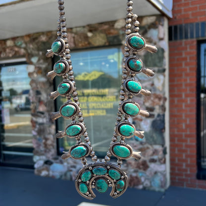 A silver Kingman turquoise squash blossom necklace.  The necklace is made with handmade Navajo pearls.