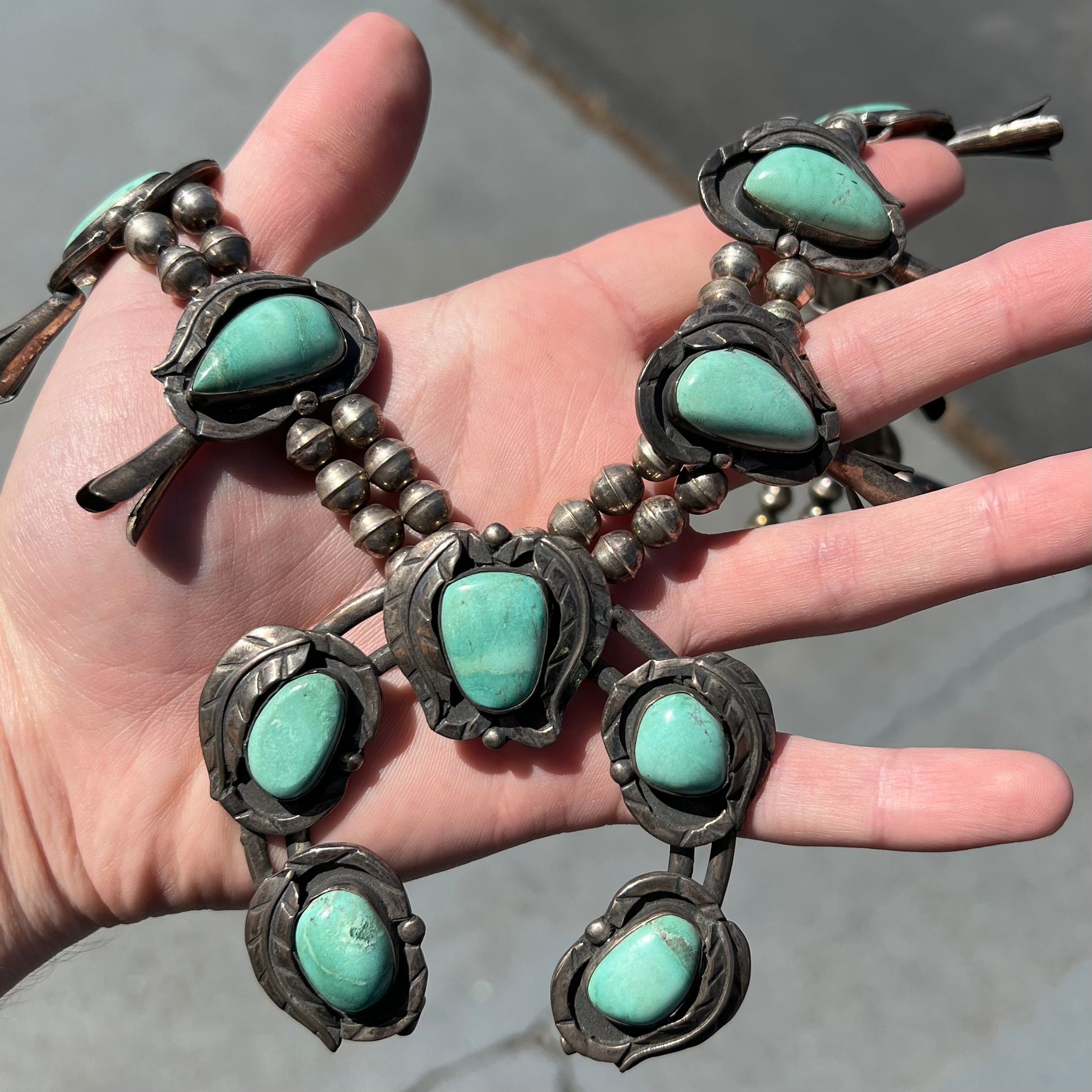 A handmade silver Navajo style squash blossom necklace set with green Kingman turquoise.
