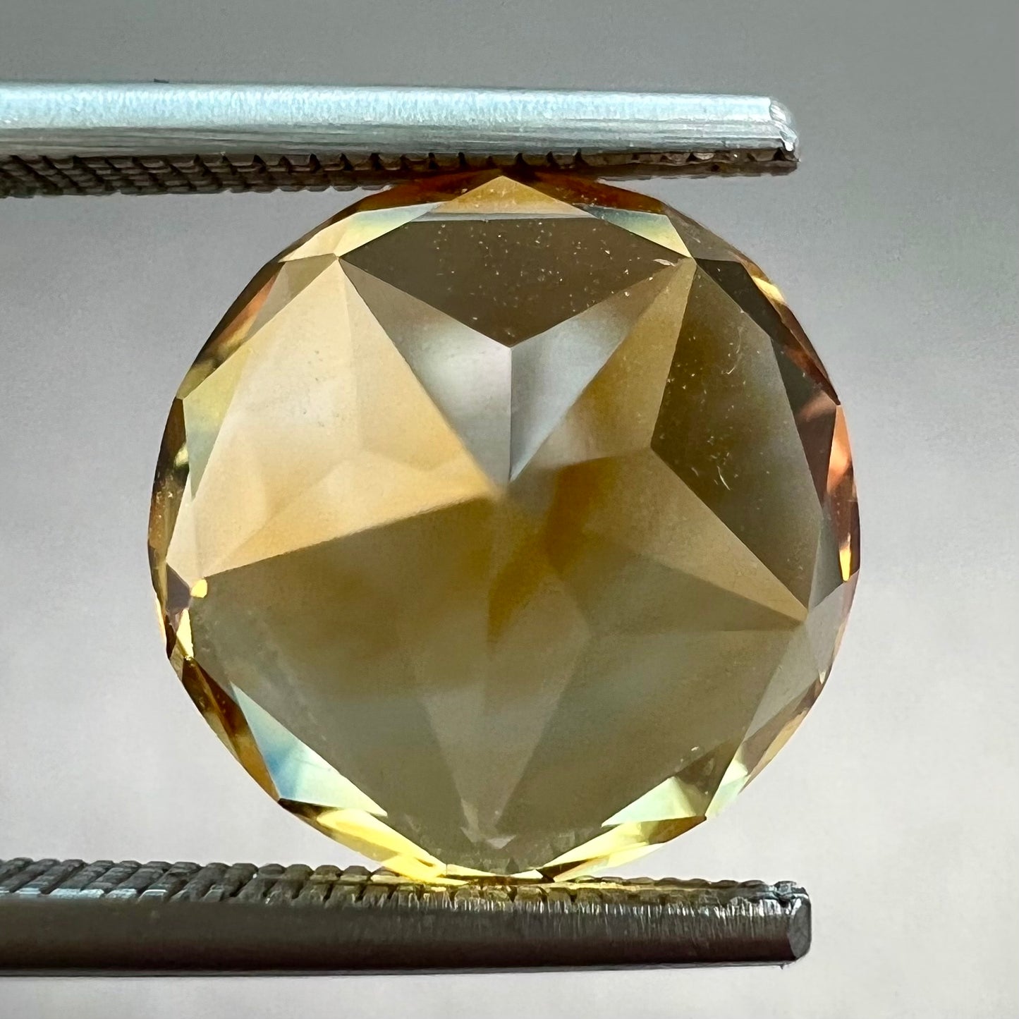 A loose, faceted round cut citrine stone with back facets that form a five pointed star.