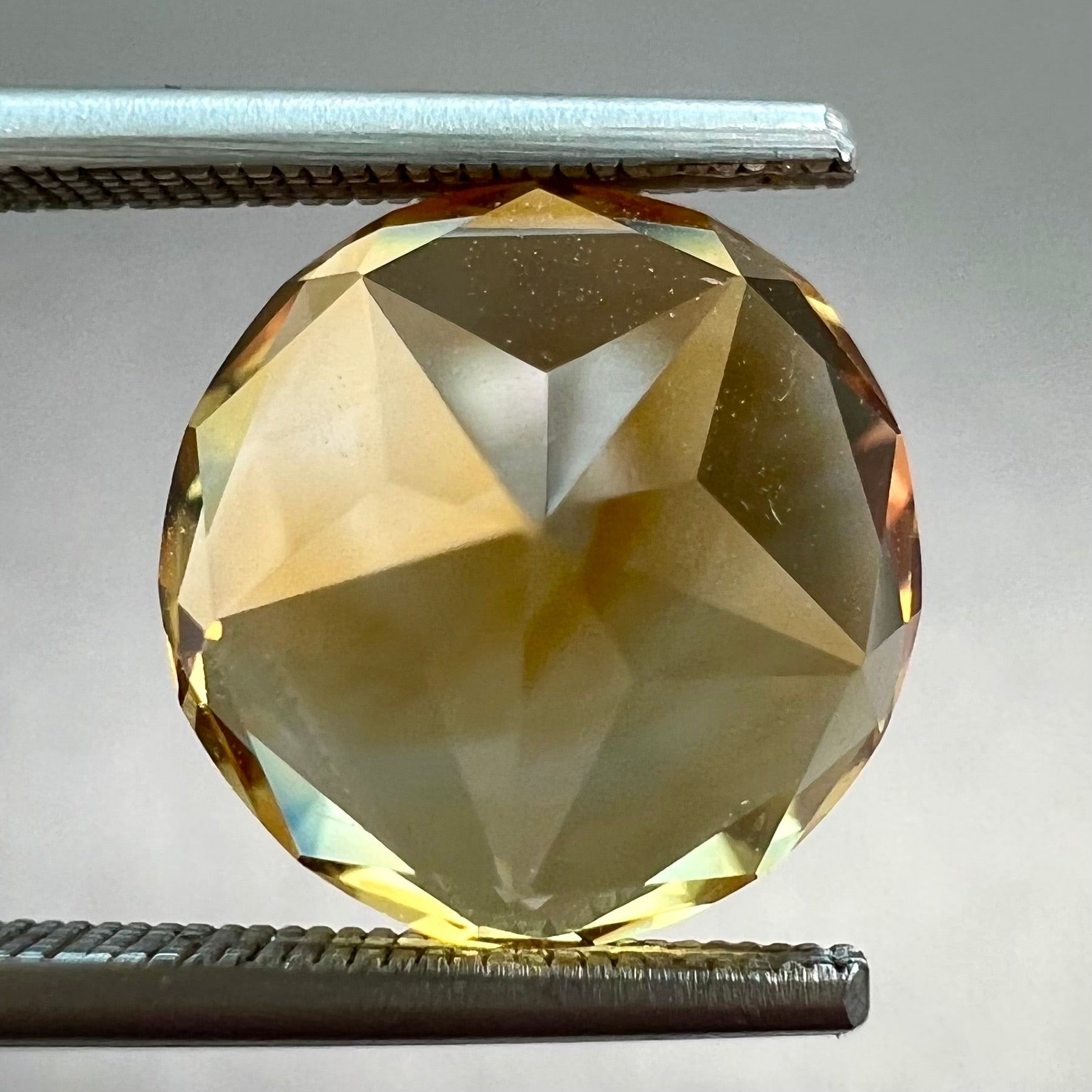 A loose, faceted round cut citrine stone with back facets that form a five pointed star.