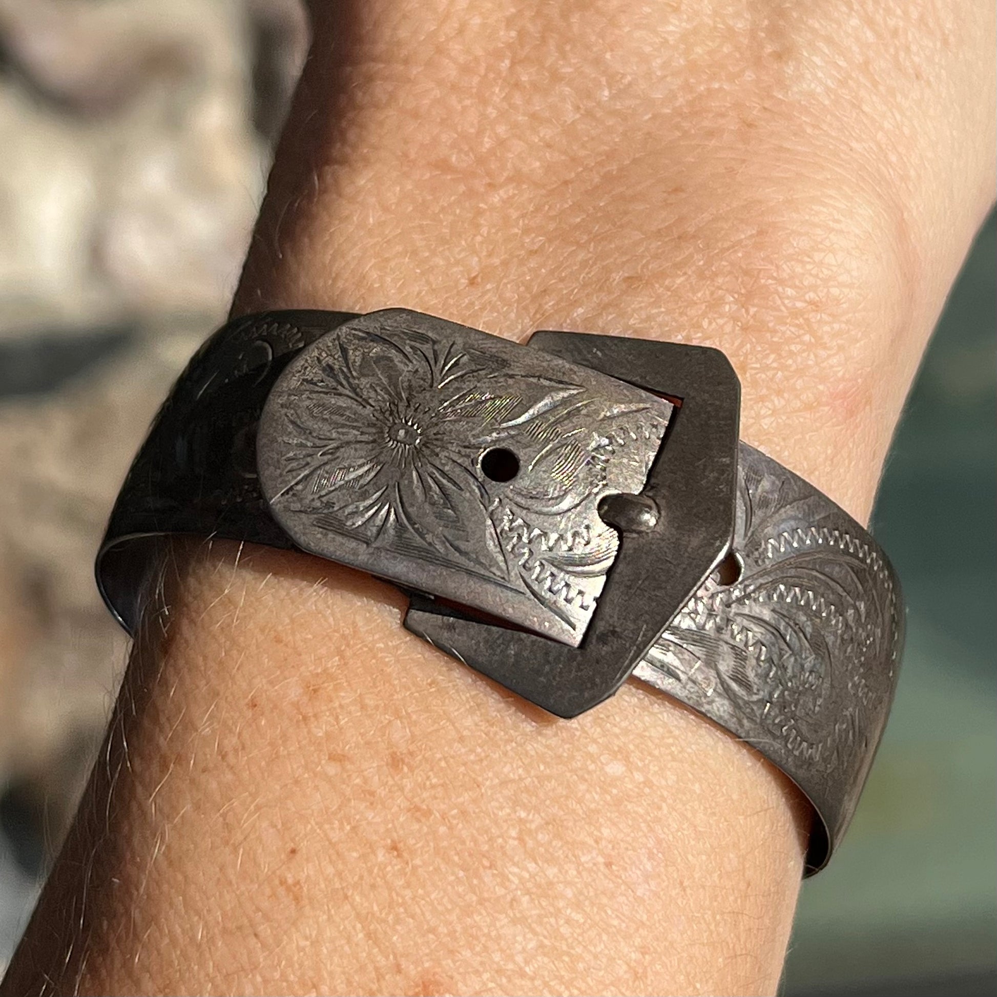 A photo showing a sterling silver antique Art Nouveau buckle bracelet.  The bracelet is engraved and etched with a floral pattern design.  The piece is being displayed on a person's wrist.