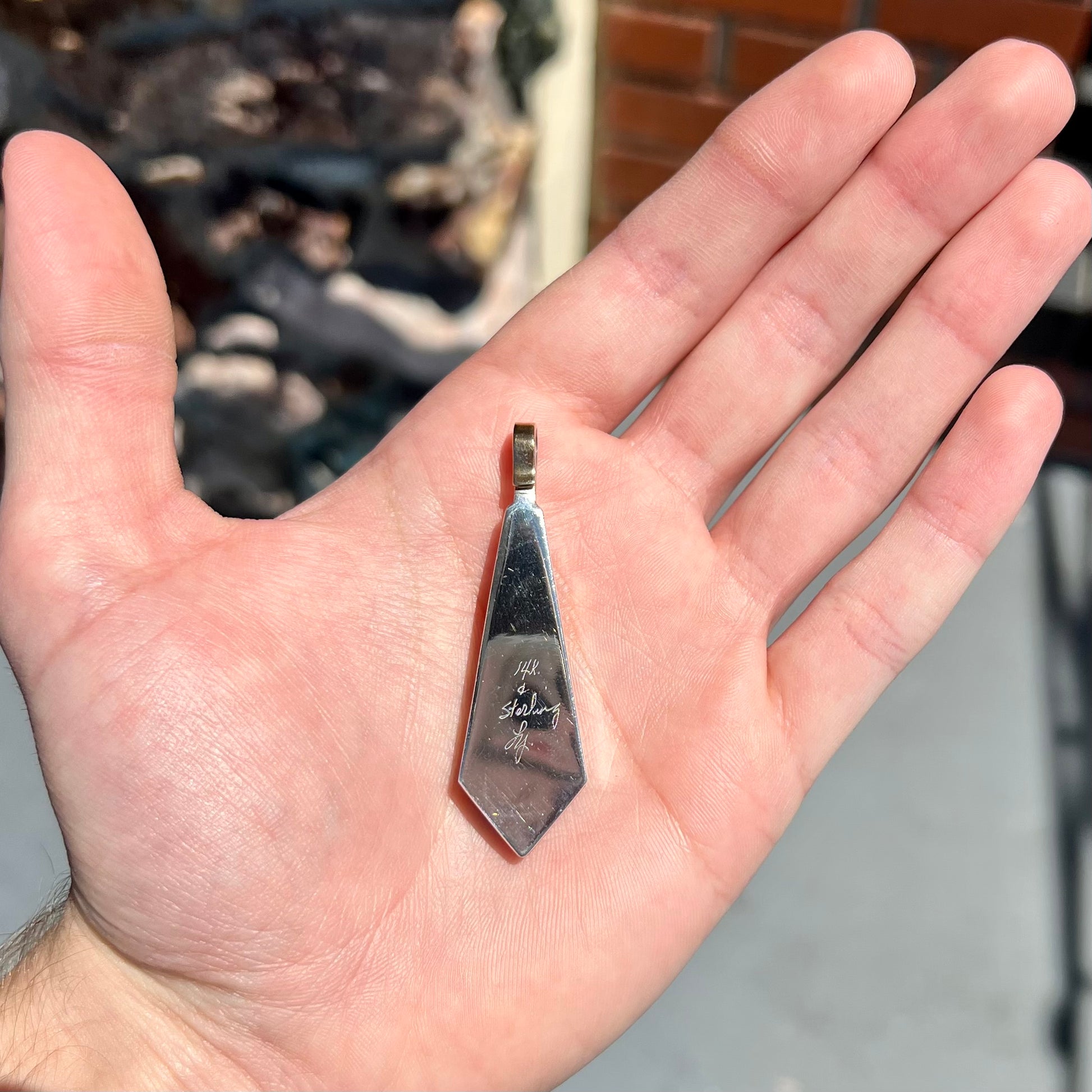 A yellow gold and sterling silver pendant inlaid with turquoise, coral, and lapis lazuli stones.  The piece is made by an unknown Native American artist and signed with the initials "LY".