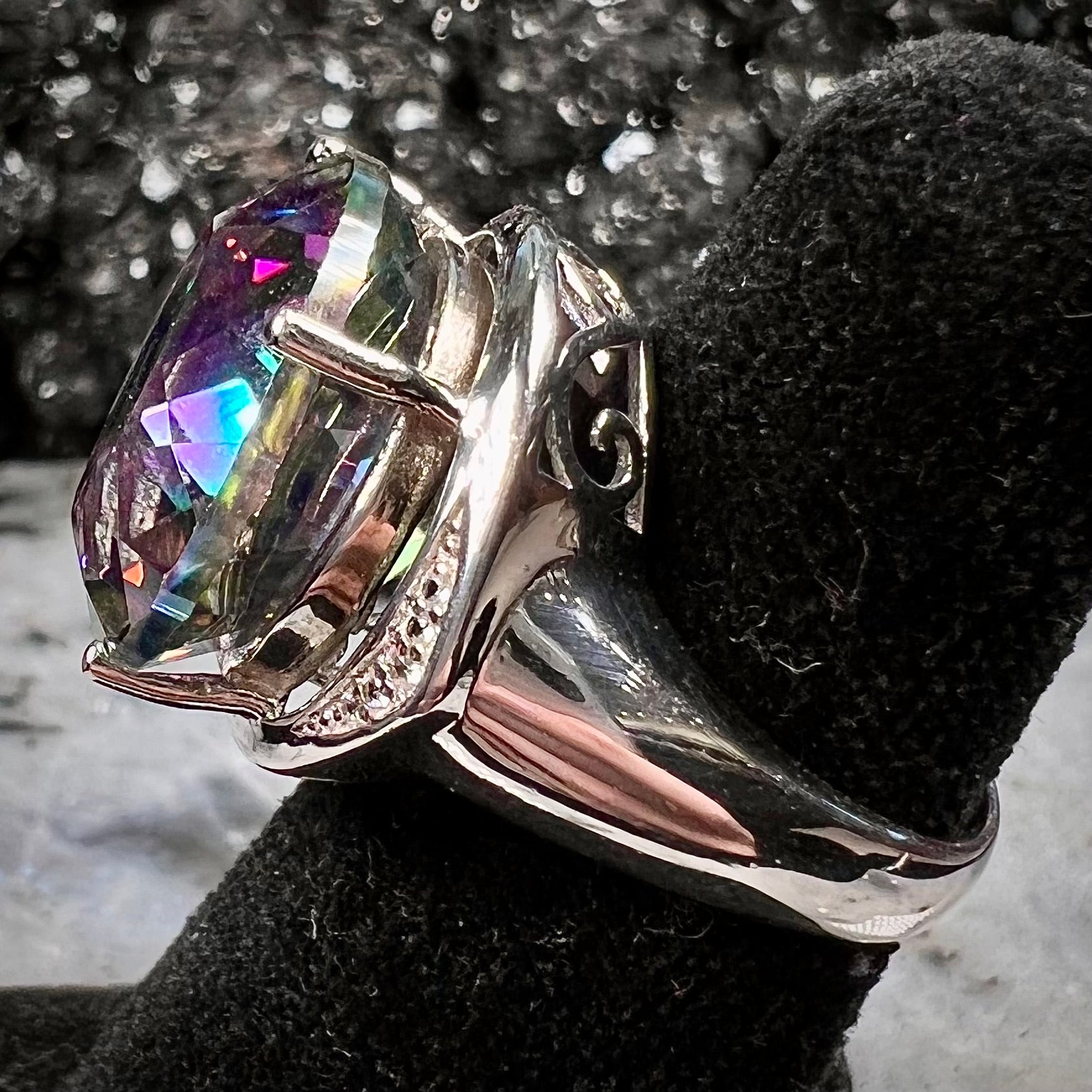 A large, round cut pink and green mystic topaz set in a sterling silver ring with white topaz accent stones.
