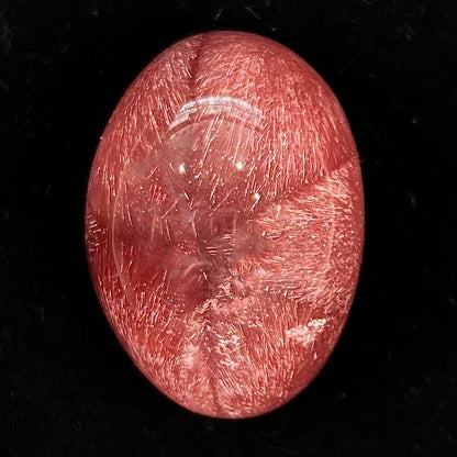 A large, oval cabochon cut strawberry quartz.  The stone has a trapiche star-like pattern.