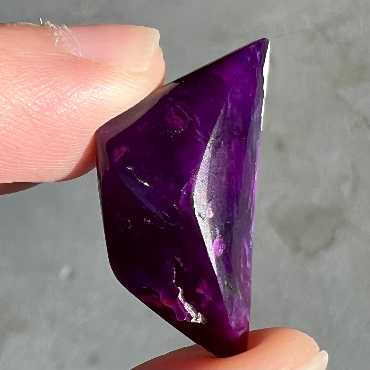 A freeform cabochon cut piece of dark purple sugilite.