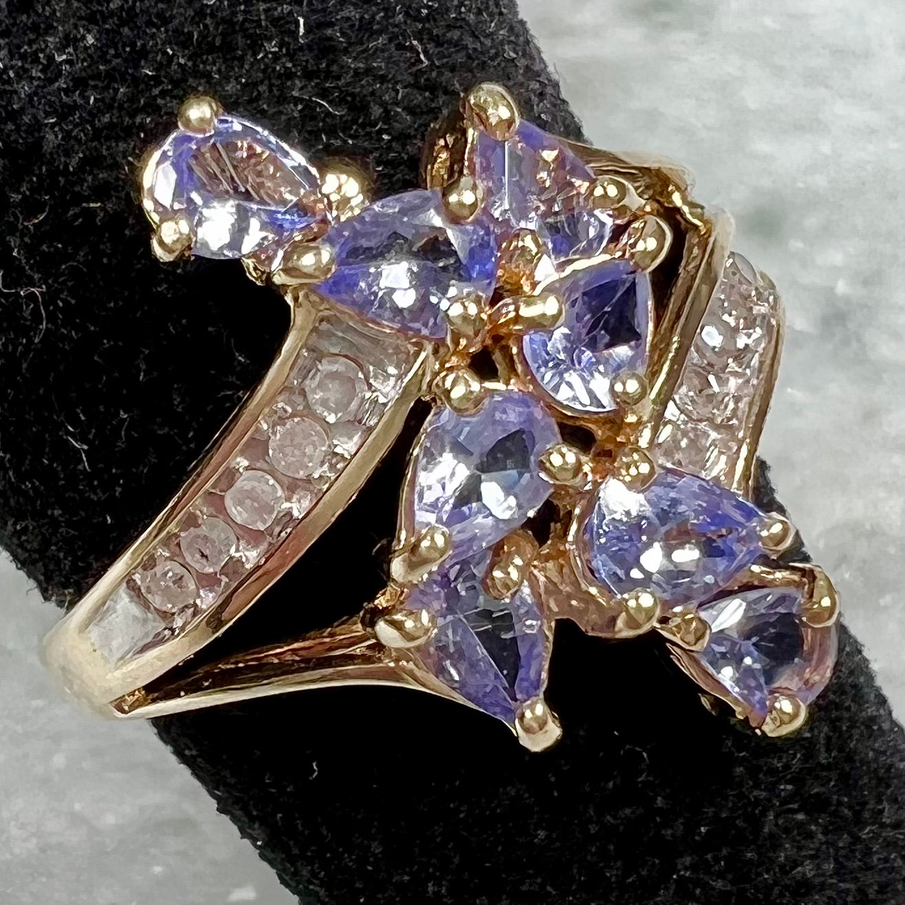 A pear shape tanzanite cluster ring channel set with diamonds in yellow gold.