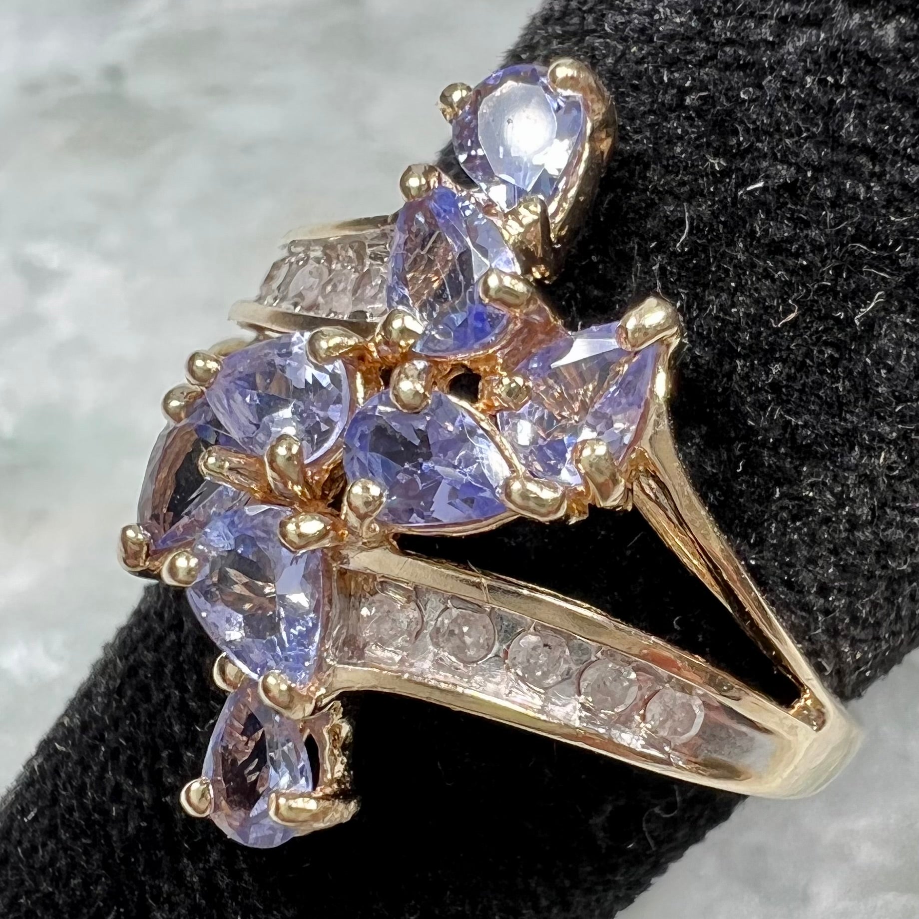 A pear shape tanzanite cluster ring channel set with diamonds in yellow gold.