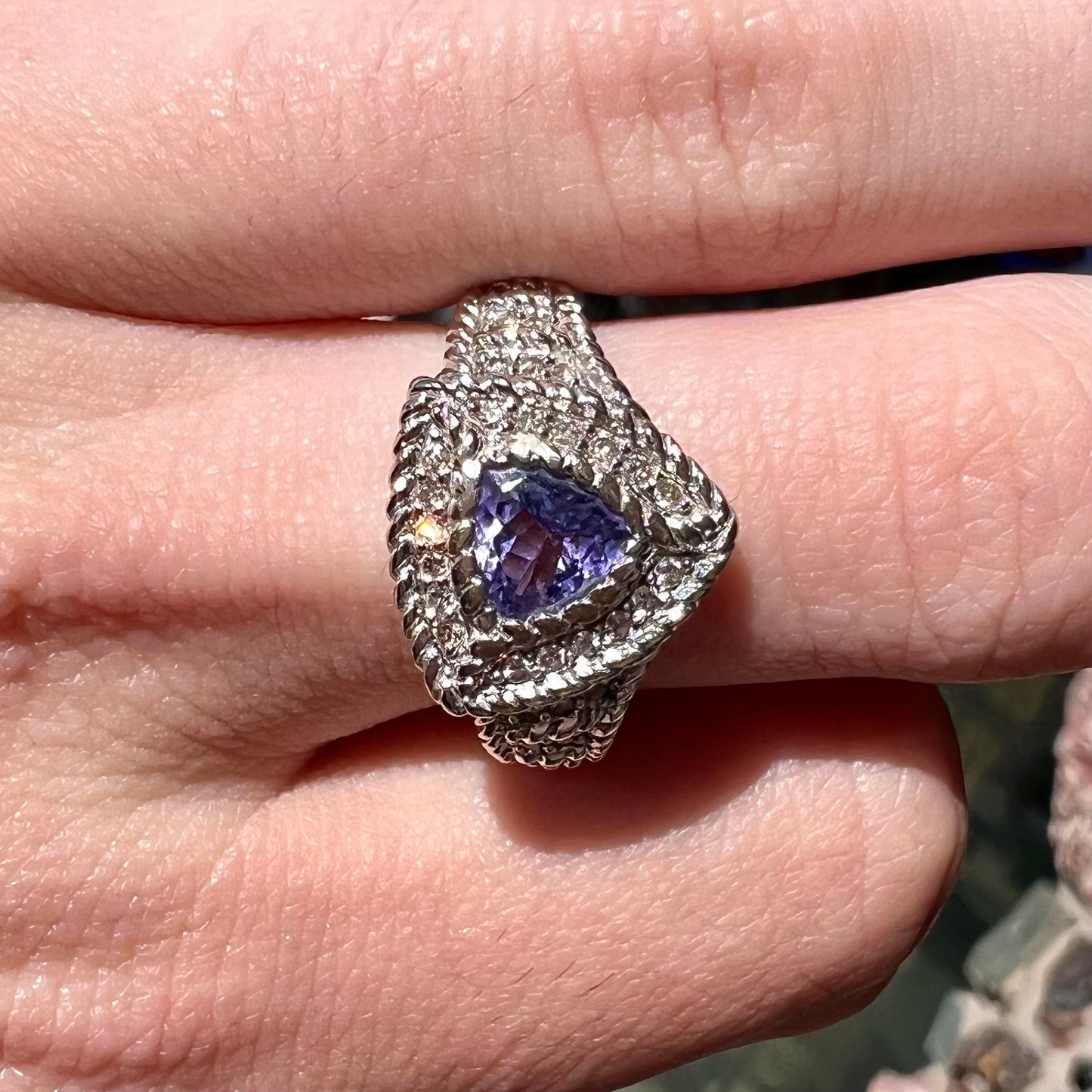 A white gold trillion cut tanzanite ring set with a diamond halo and diamond accents.