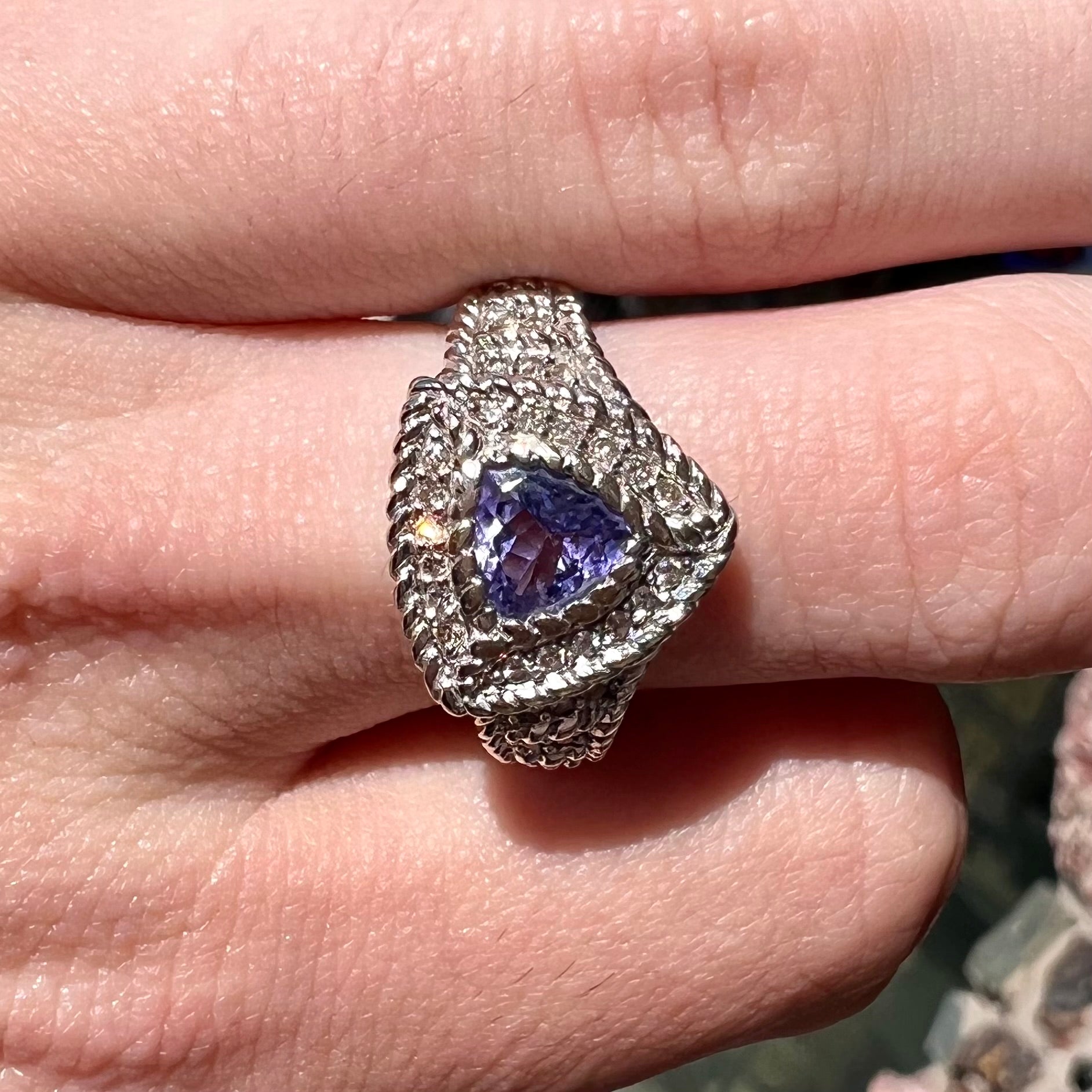 A white gold trillion cut tanzanite ring set with a diamond halo and diamond accents.