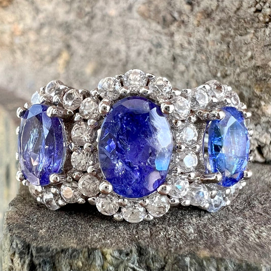 A sterling silver past, present, future three stone tanzanite ring.  The main stones are set in a halo of cubic zirconia.