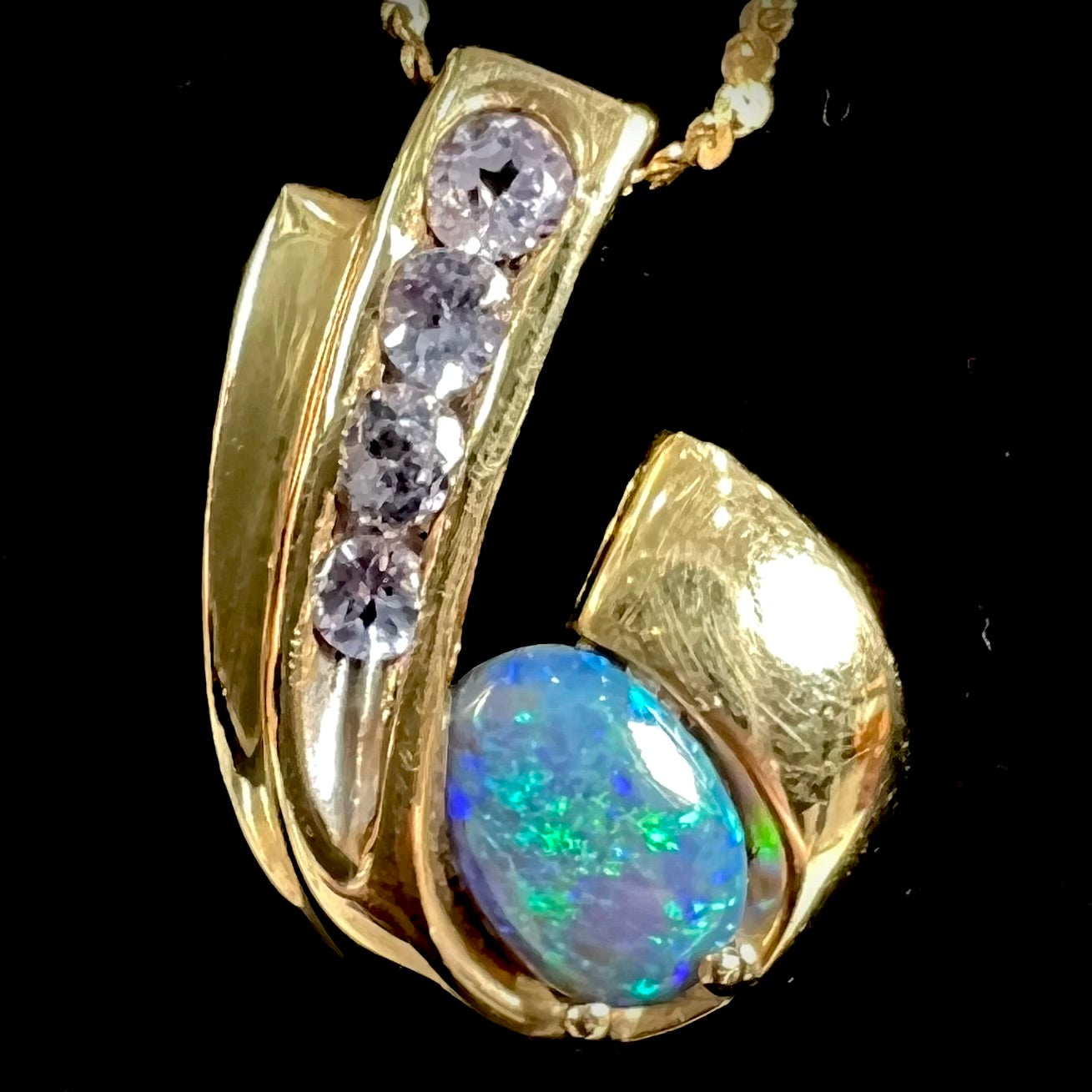 A Lightning Ridge black crystal opal necklace set with blue tanzanite in yellow gold.  Gold chain not included.