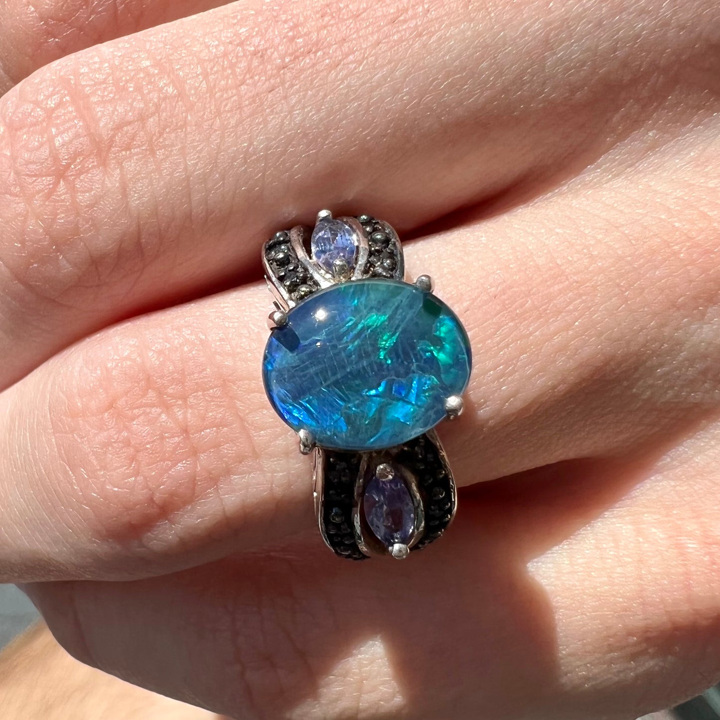 A sterling silver ring set with a black opal triplet, two marquise cut tanzanites, and round black spinel accent stones.