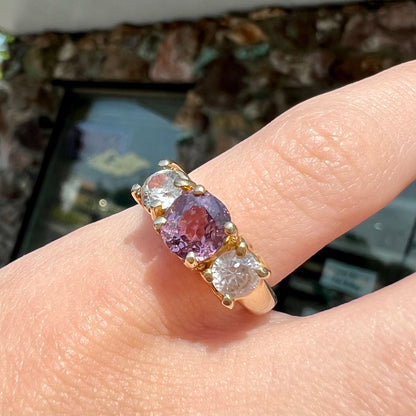A yellow gold three stone ring set with two round cut white zircons and one cushion cut purple spinel.