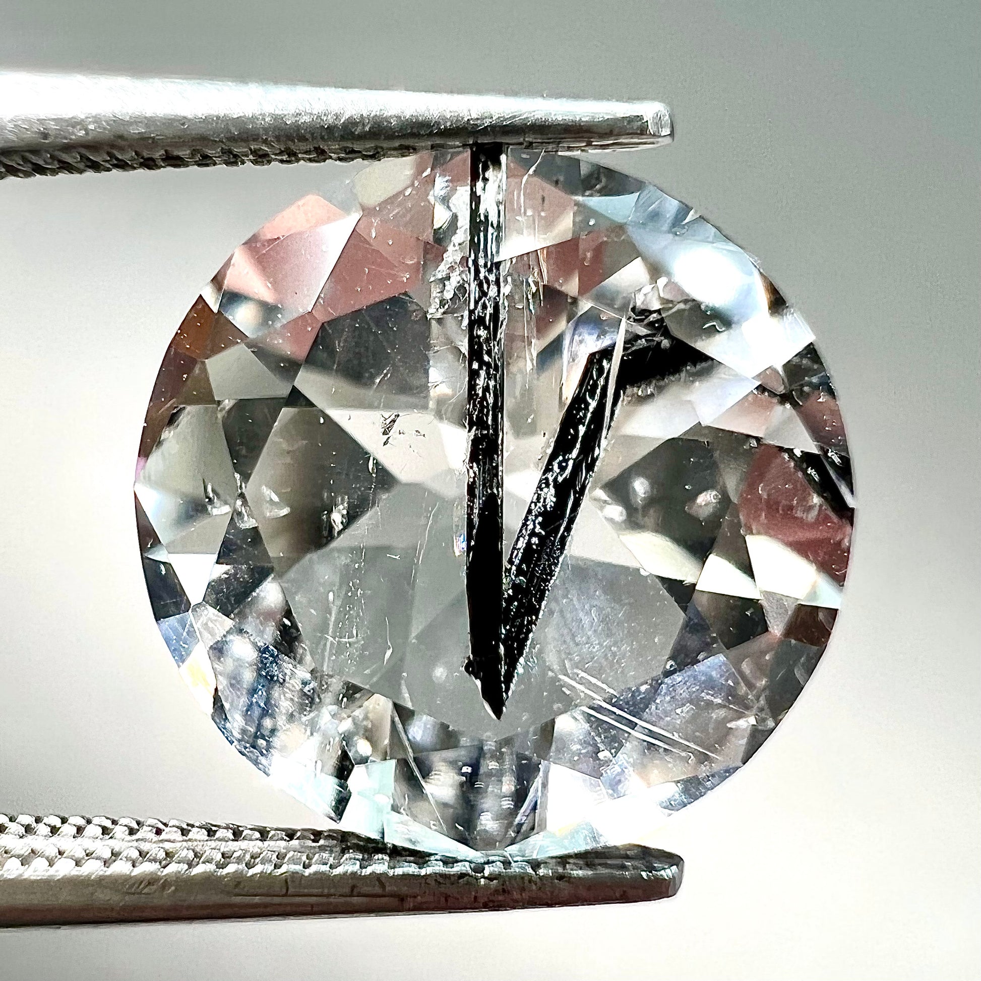 A round brilliant cut clear quartz stone with two black tourmaline crystal inclusions.