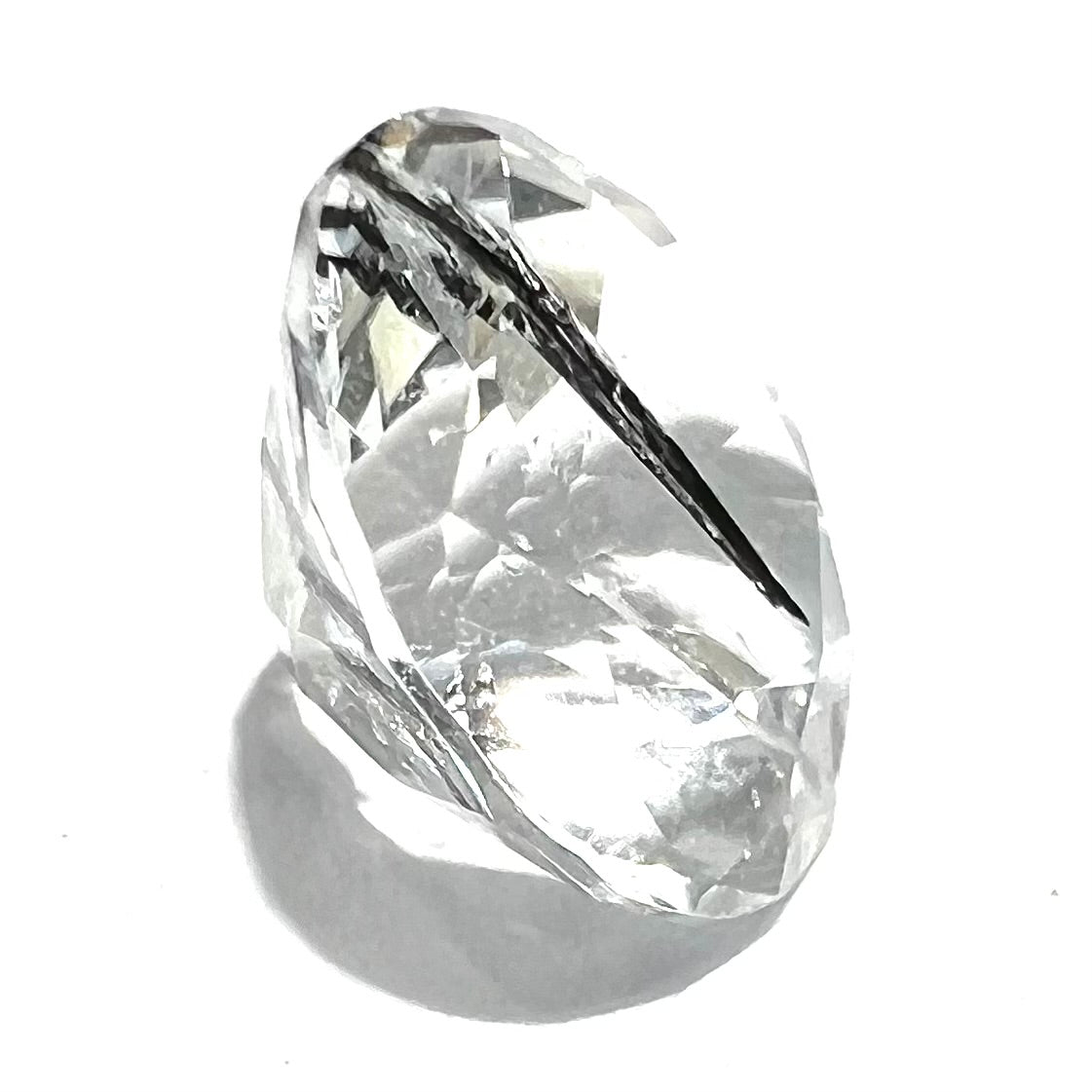 A faceted round brilliant cut clear quartz stone with black tourmaline inclusions.  Inclusions appear like a clock's hands.