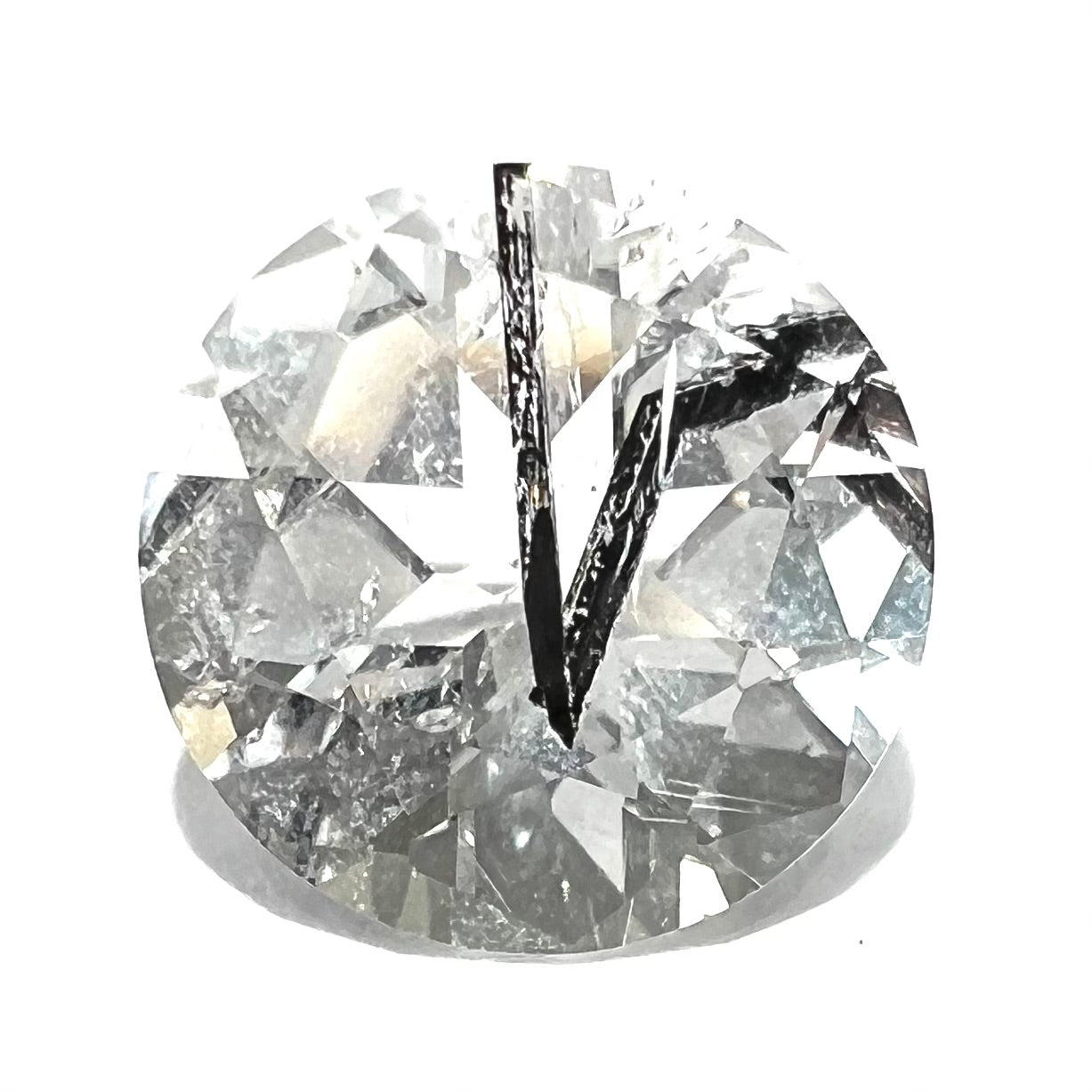 A faceted round brilliant cut clear quartz stone with black tourmaline inclusions.  Inclusions appear like a clock's hands.