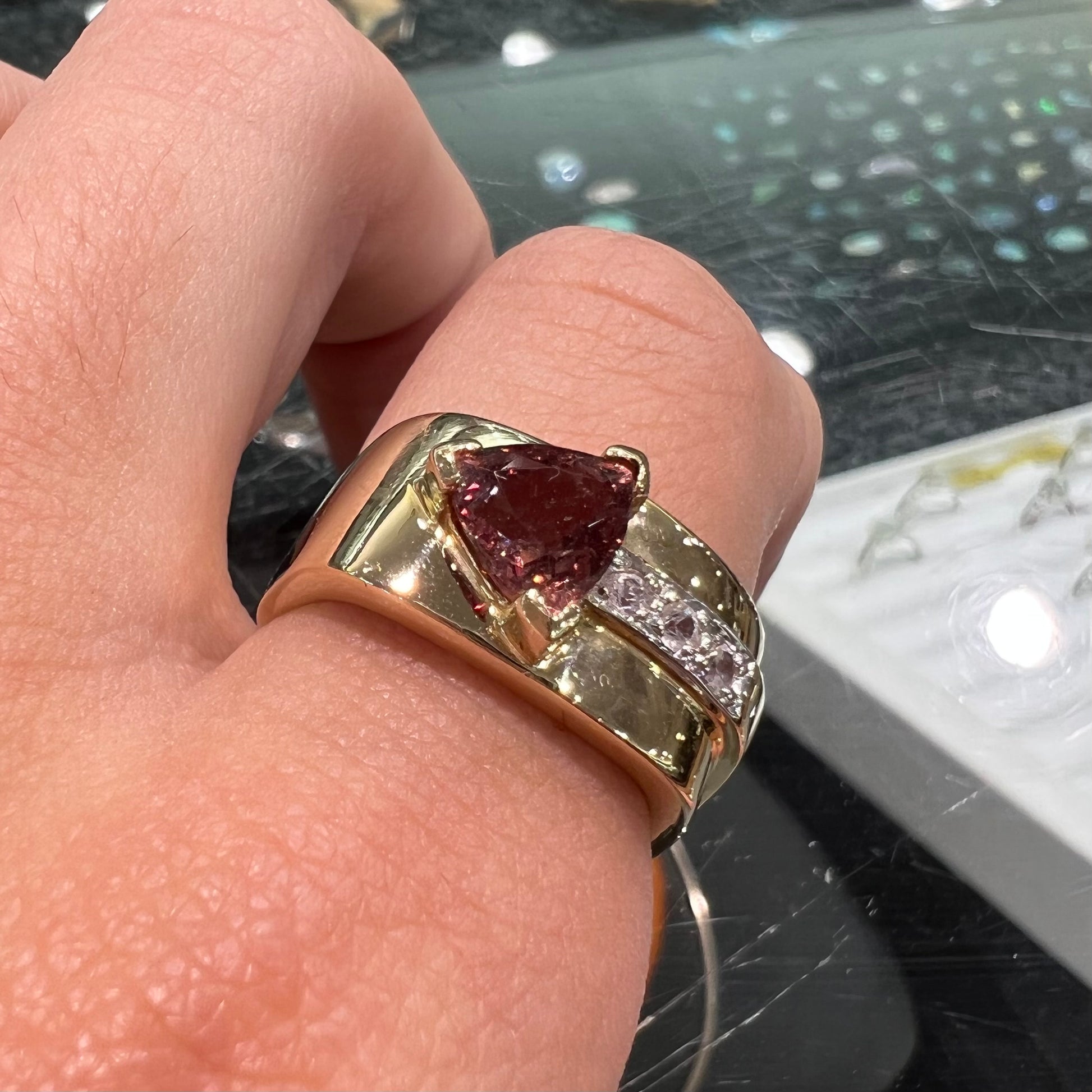 A men's gold pink tourmaline ring.  Set next to the trillion cut tourmaline is a row of three round white sapphires.