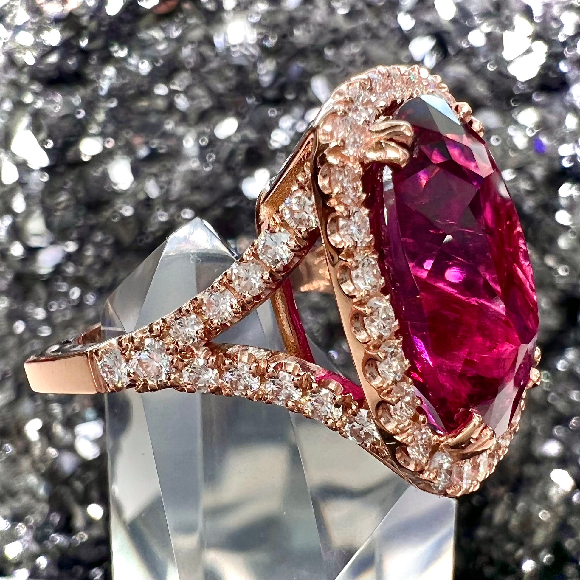 A rose gold, split shank engagement ring set with a cushion cut rubellite tourmaline in a diamond halo.