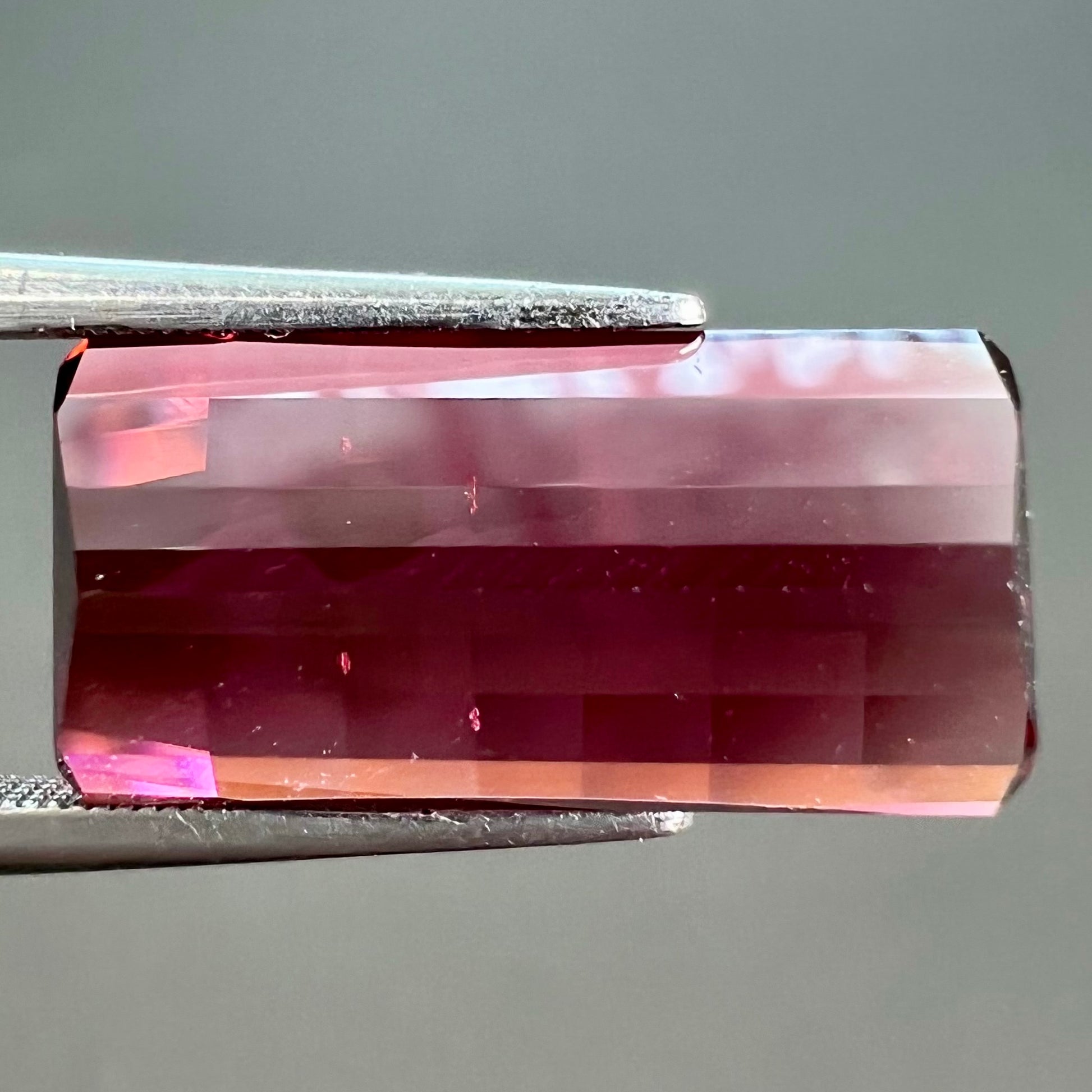 A loose, fantasy cut reddish colored tourmaline.  The cut reflects light in a way that resembles digital pixels on a screen.