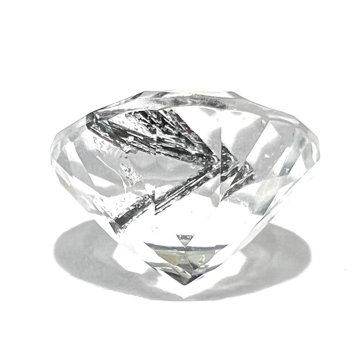 A faceted round brilliant cut clear quartz stone with black tourmaline inclusions.  Inclusions appear like a clock's hands.