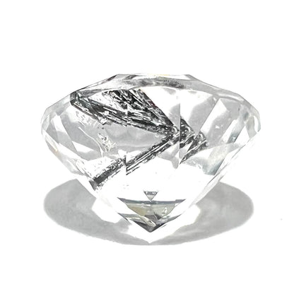 A faceted round brilliant cut clear quartz stone with black tourmaline inclusions.  Inclusions appear like a clock's hands.