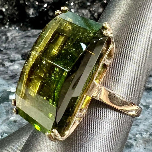 A faceted step-cut dark green tourmaline basket set solitaire ring cast in yellow gold.